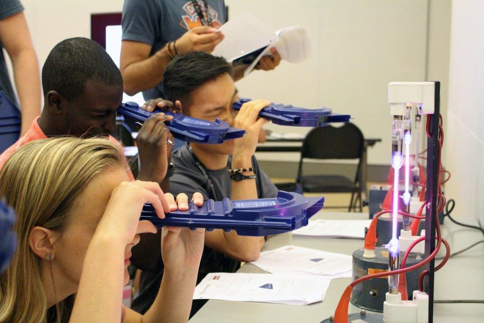 Three QSYS participants looking through spectrometers at an elemental emission source