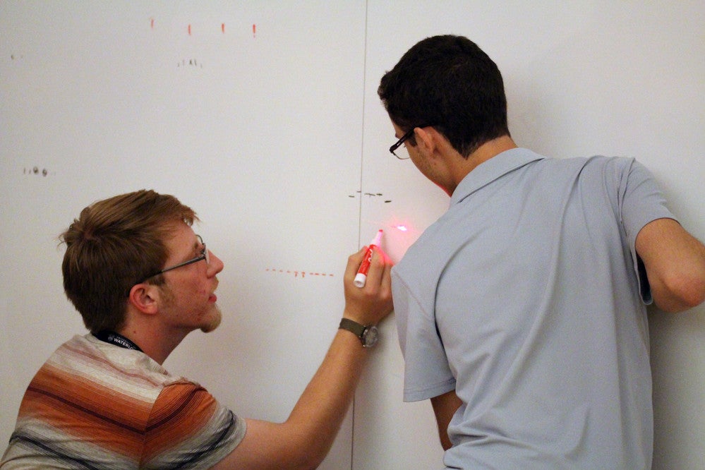 Students measure a laser on the wall.