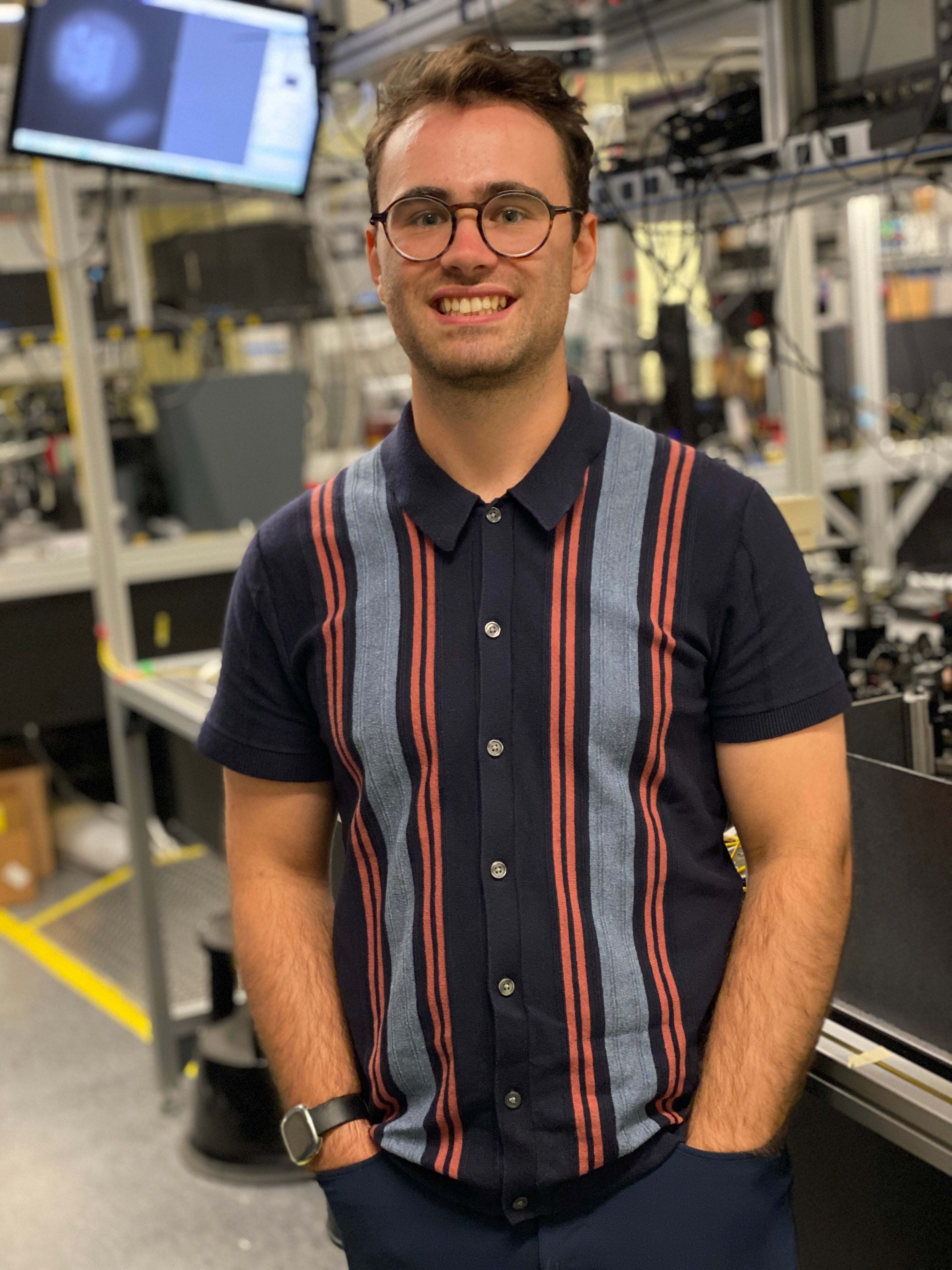 A man wearing glases and a striped shirt standing in front of quantum instruments