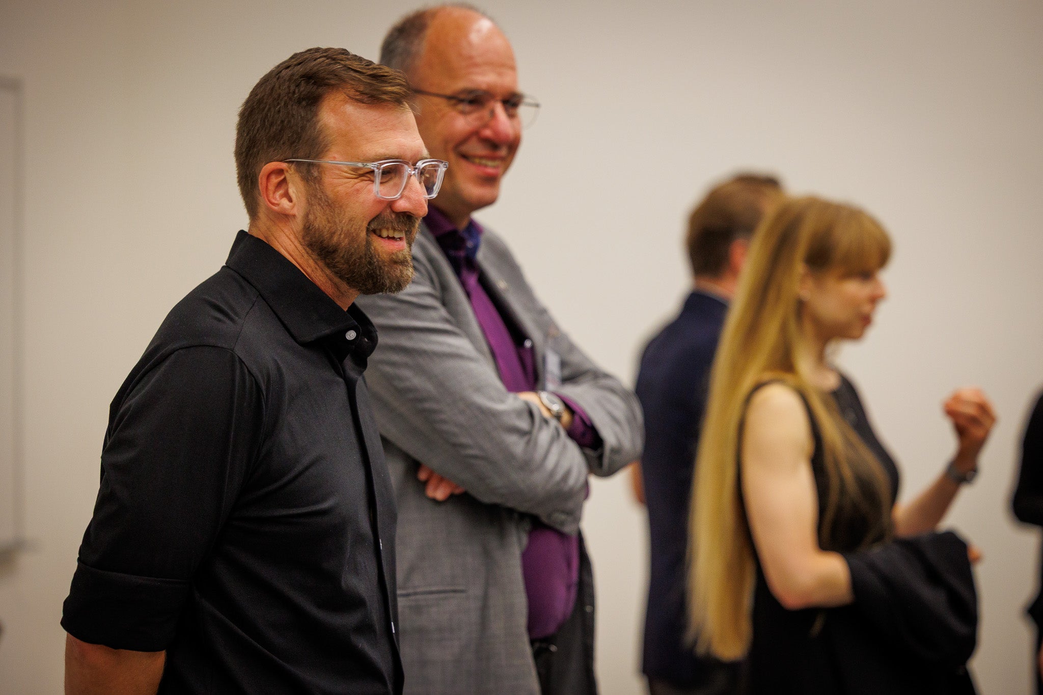 Two men at the forefront smiling and a woman in the background talking