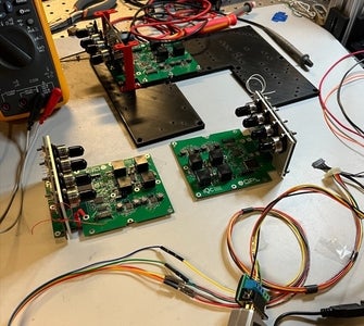 The electronics board resting on a black 3D printed base about the size of the satellite bus. Optical fibre connectors are visible on the vertical boards where the detectors will be placed. 