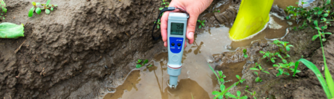 A person wearing rubber boots standing in water and using a probe to test the water