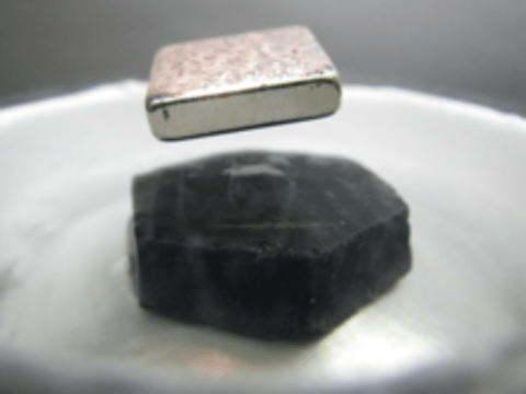 a square magnet levitating over a black chunk of superconductive material sitting in a dish of liquid nitrogen