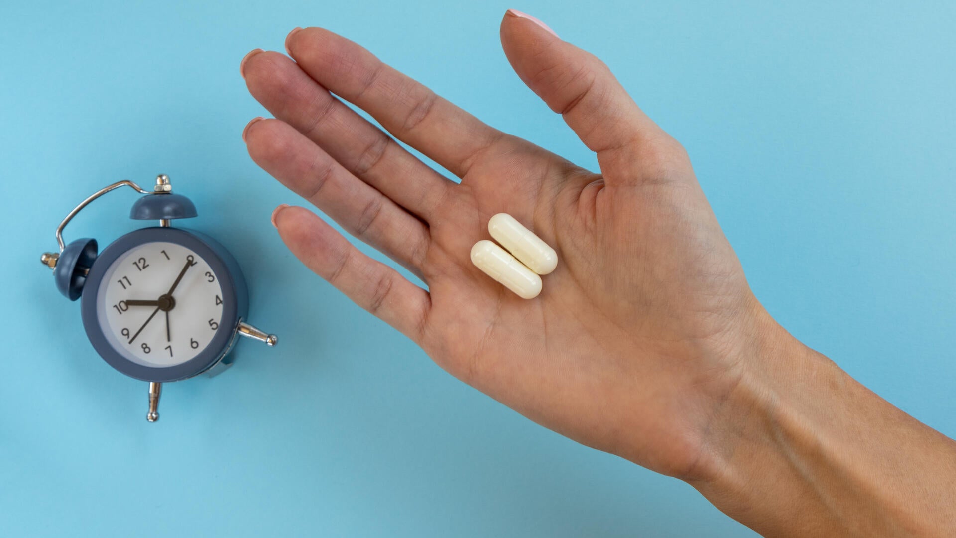 Image of hand holding pills with a clock
