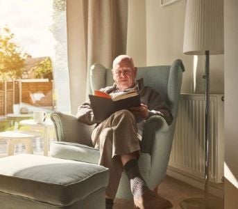Older man reading book in green armchair