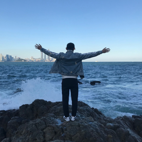 a student stands with arms open in front of the ocean