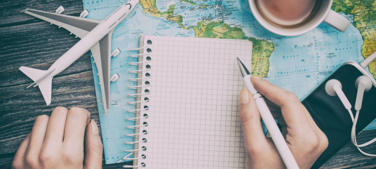 Person writing in notebook with a coffee, a small plane and a world map.