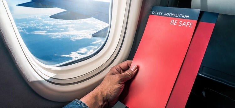 Person holding a safety pamphlet by an airplane window