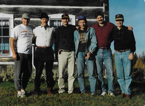Six smiling men pose for group photo at cottage.