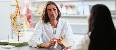 Student wearing lab coat talks to teaching assistant in the human anatomy lab.