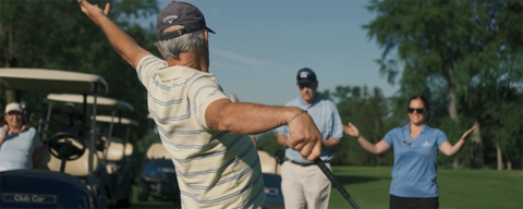 Older man playing golf with his hands in the air while other golfers watch.