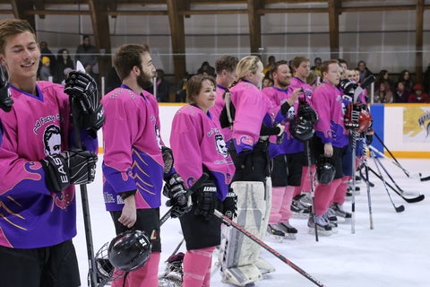 Hockey players in pink jerseys, line up on the blue line. 
