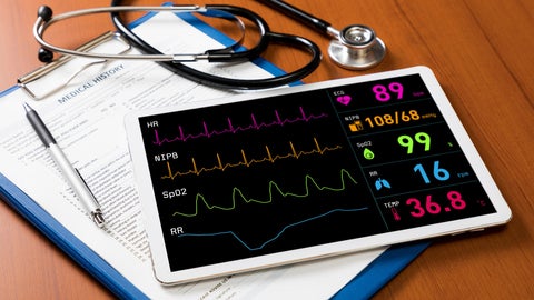 Image of an ipad with heart monitor information on it beside medical tools and clipbaord