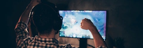Man looking at computer game raises his arms in victory.