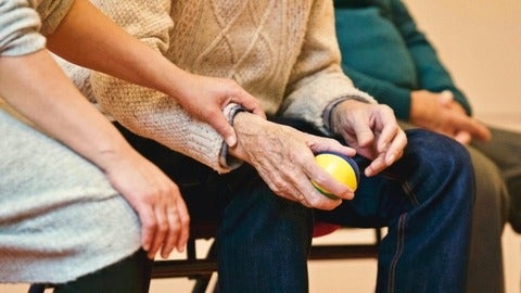 Old person holding a ball with a nurse beside him.