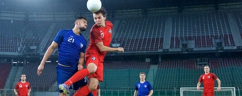 Soccer player heads ball in empty stadium.