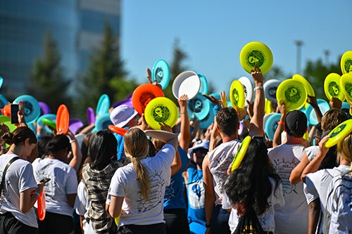 Students hold frisbees on sunny day taking Faculty pledge on orientation week.