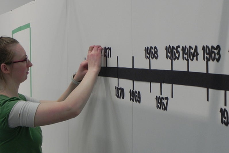 Student adding numbers to timeline on exhibit wall.