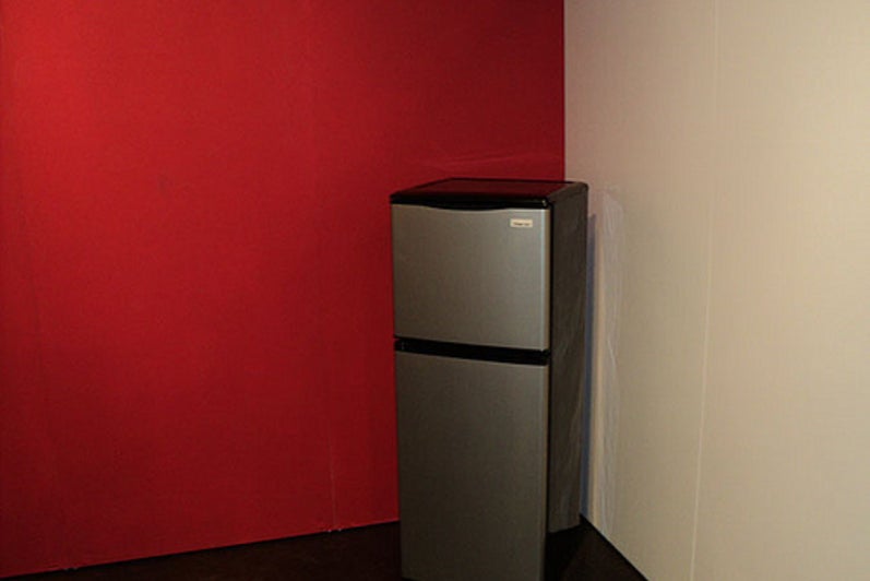 Stainless steel fridge in the corner where a red wall meets a white wall.