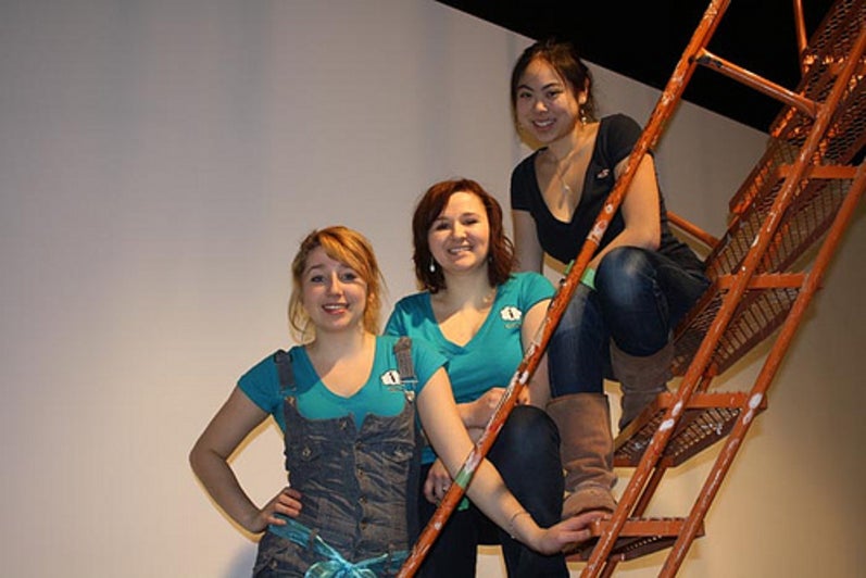 Three girls sitting on the steps of the ladder.