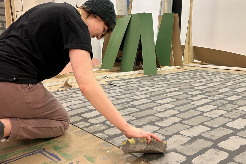 a person kneels on the floor next to a large castle stone pattern using a sponge on it