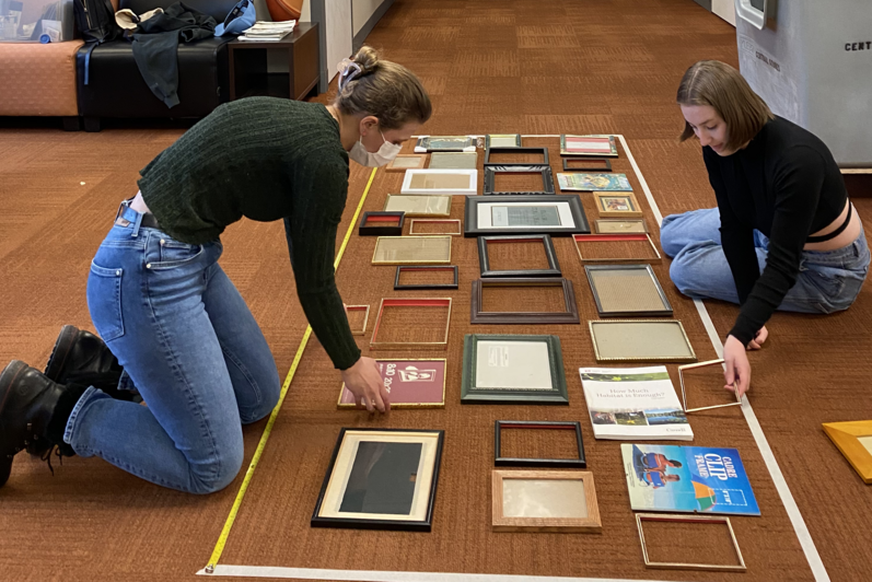 two people kneel on the floor laying out squares in a large rectangular outline