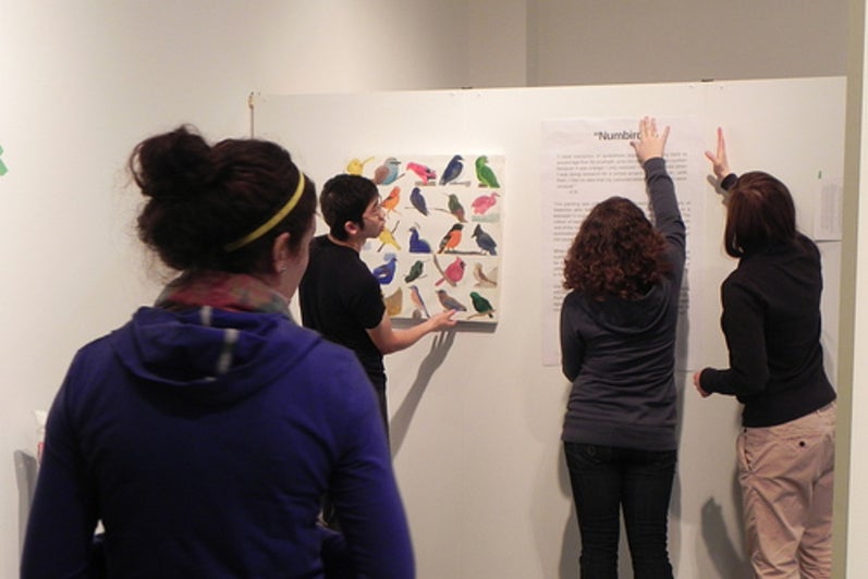 Four students placing posters on white exhibition wall.