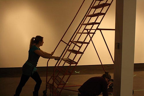 Student pushing lights-ladder across gallery.
