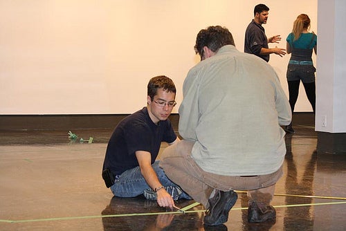Students laying down tape on gallery floor.