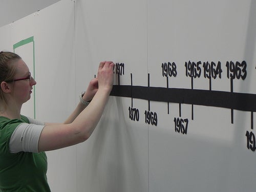 Student adding numbers to timeline on exhibit wall.