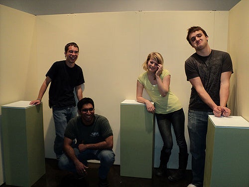 Four students pose around three green mid-height podiums.