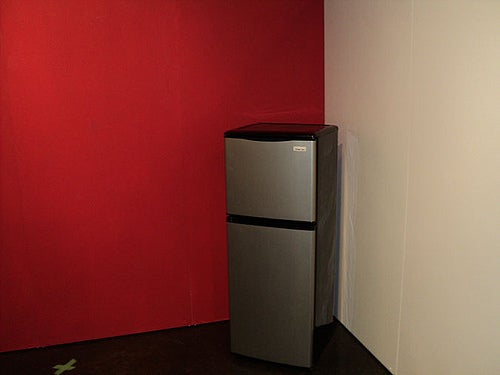 Stainless steel fridge in the corner where a red wall meets a white wall.