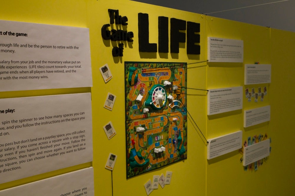"The Game of Life" sign on exhibit wall over board game diagram.