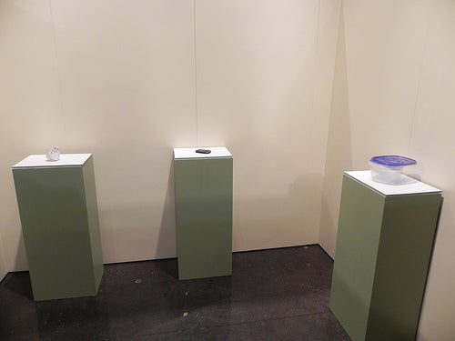 Three green podiums with a plastic gorcery bag, phone, and food container with lid on top, respectively.
