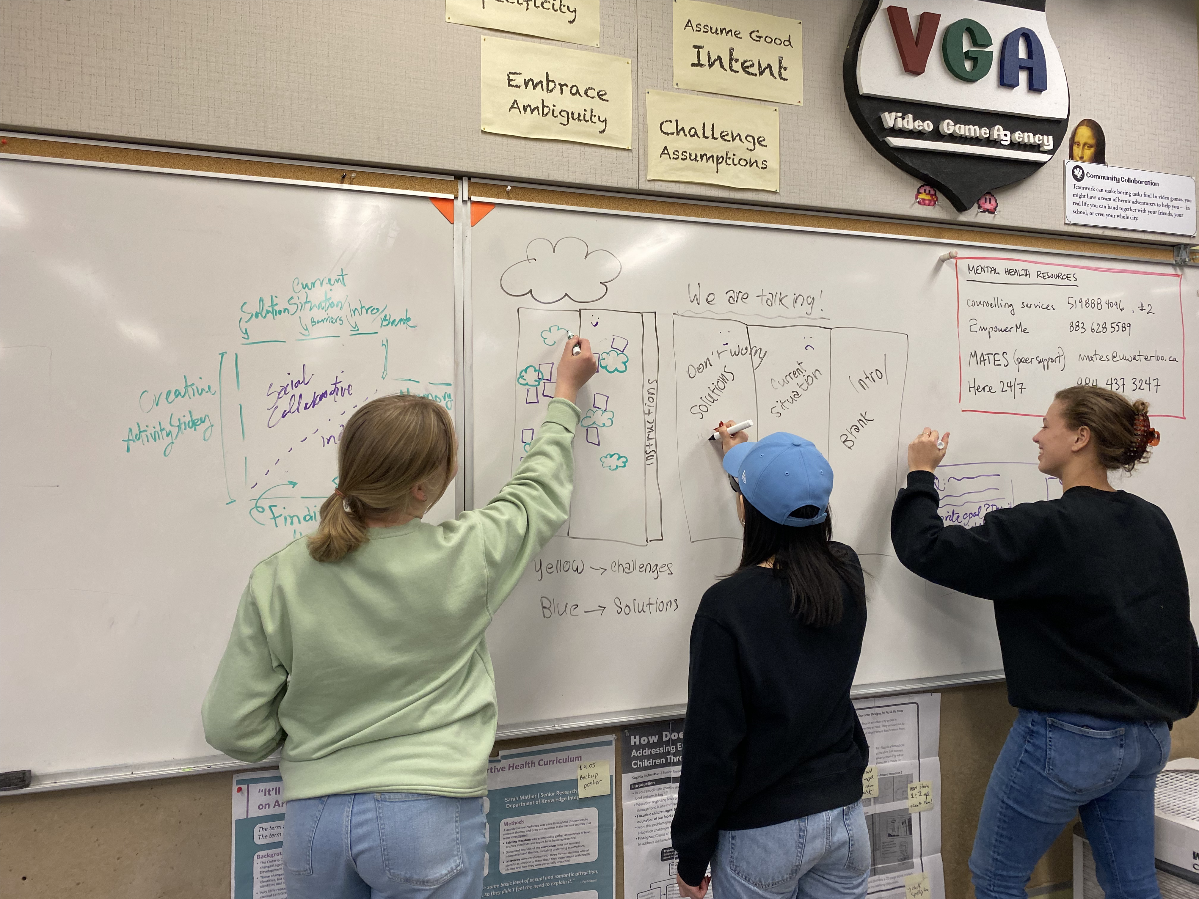 three people write notes on a large white board