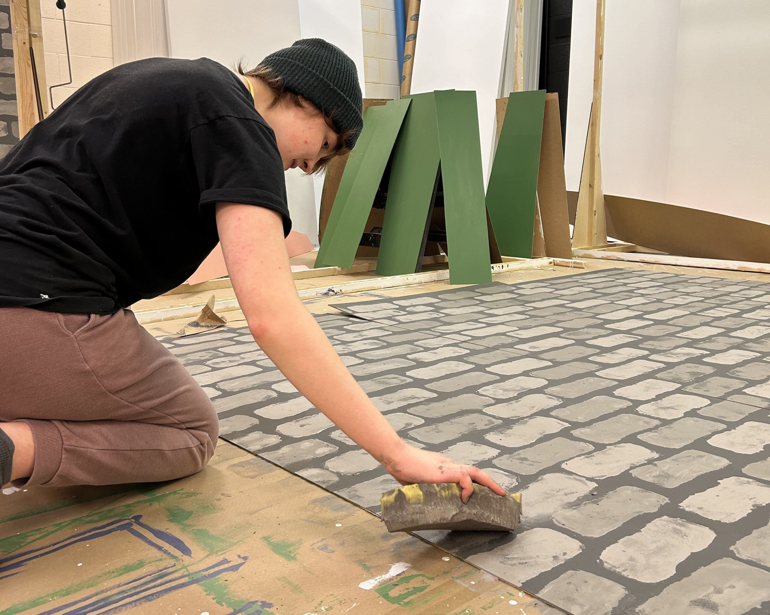 a person kneels on the floor next to a large castle stone pattern using a sponge on it