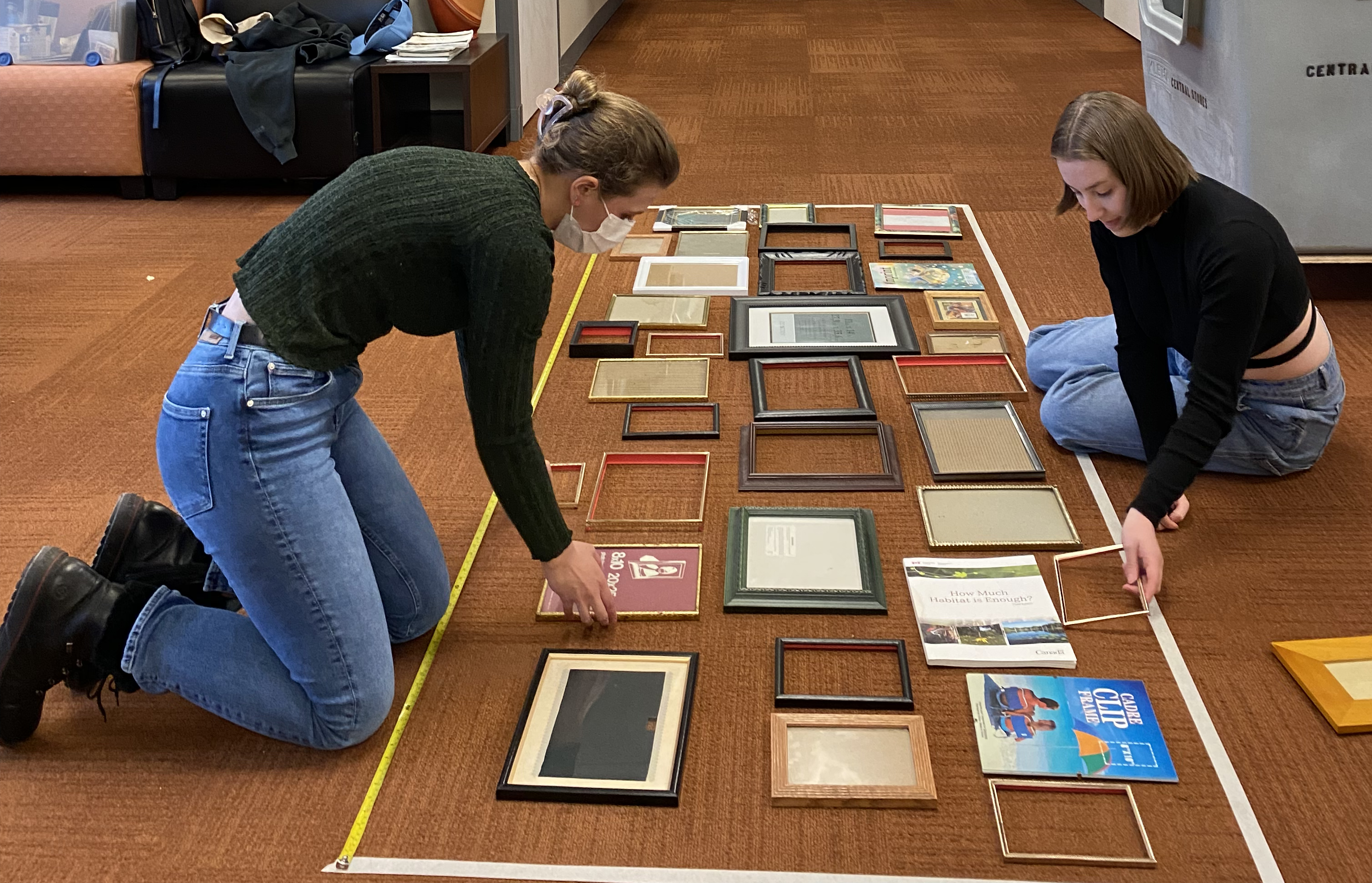 two people kneel on the floor laying out squares in a large rectangular outline