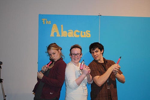 Three students pose with pink tools infront of a wall reading "The Abacus".