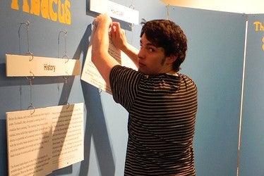Domenic hanging a white information board on exhibit wall.
