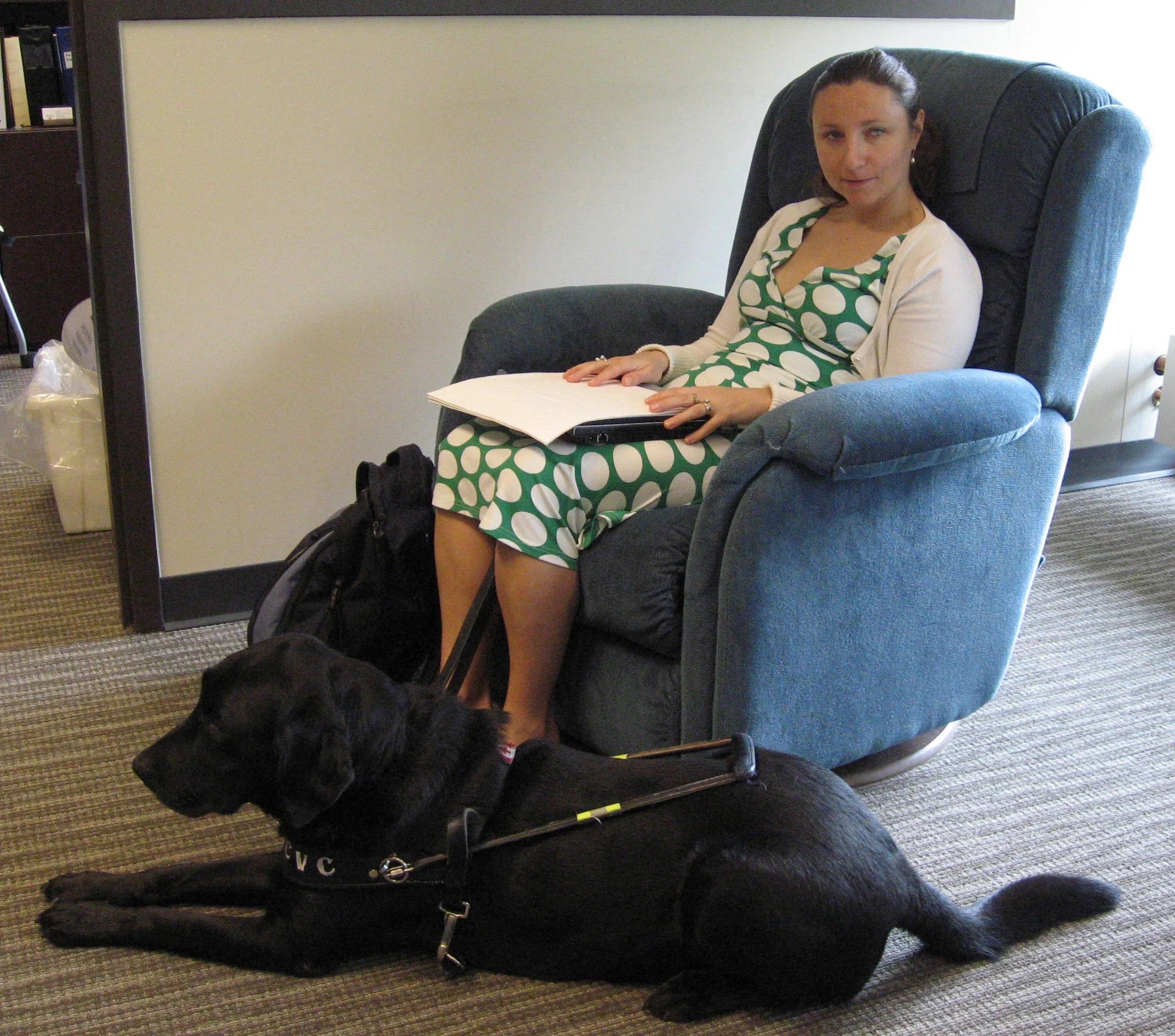 Student reading her braille document while sitting on the most comfortable chair on campus. Her guide dog is at her feet.