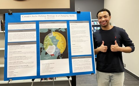 A person stands beside a large academic research poster titled “Canada’s Arctic Defence Strategy in a Changing Arctic” displayed on an easel indoors
