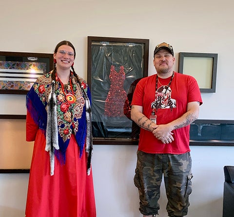 Two people standing next to a dress made of red beads
