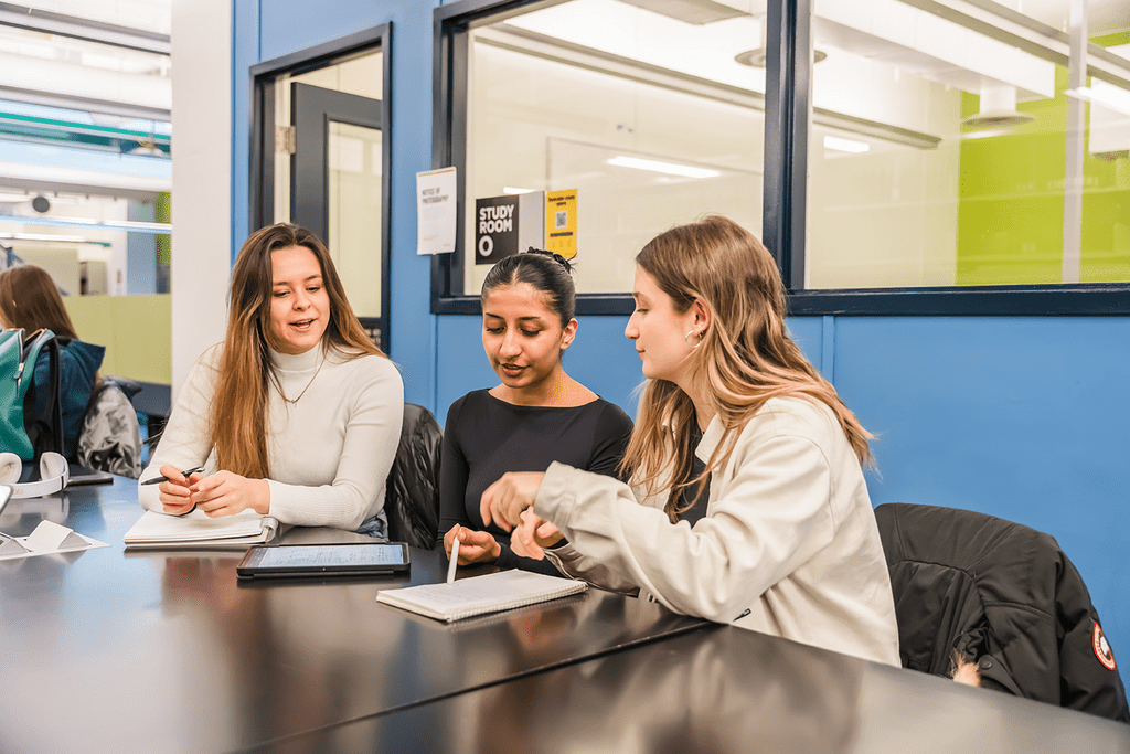 Three people are sitting around a table in a study area.