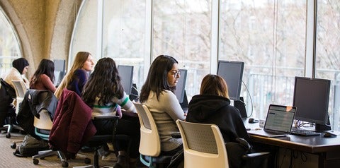 Students seated at desks with laptops facing a window