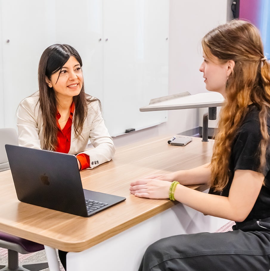 two women talking at a table with a laptop between them
