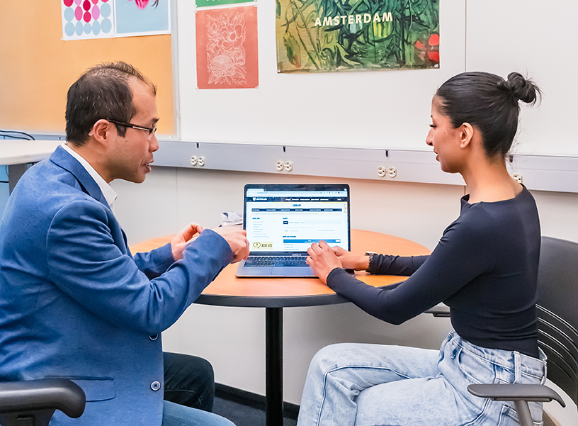 a university student sitting at a table talking with a librarian