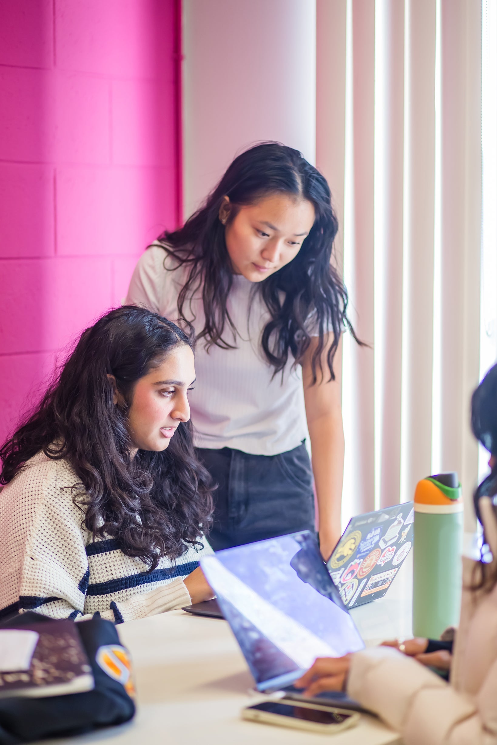 two women collaborating at a table with laptops