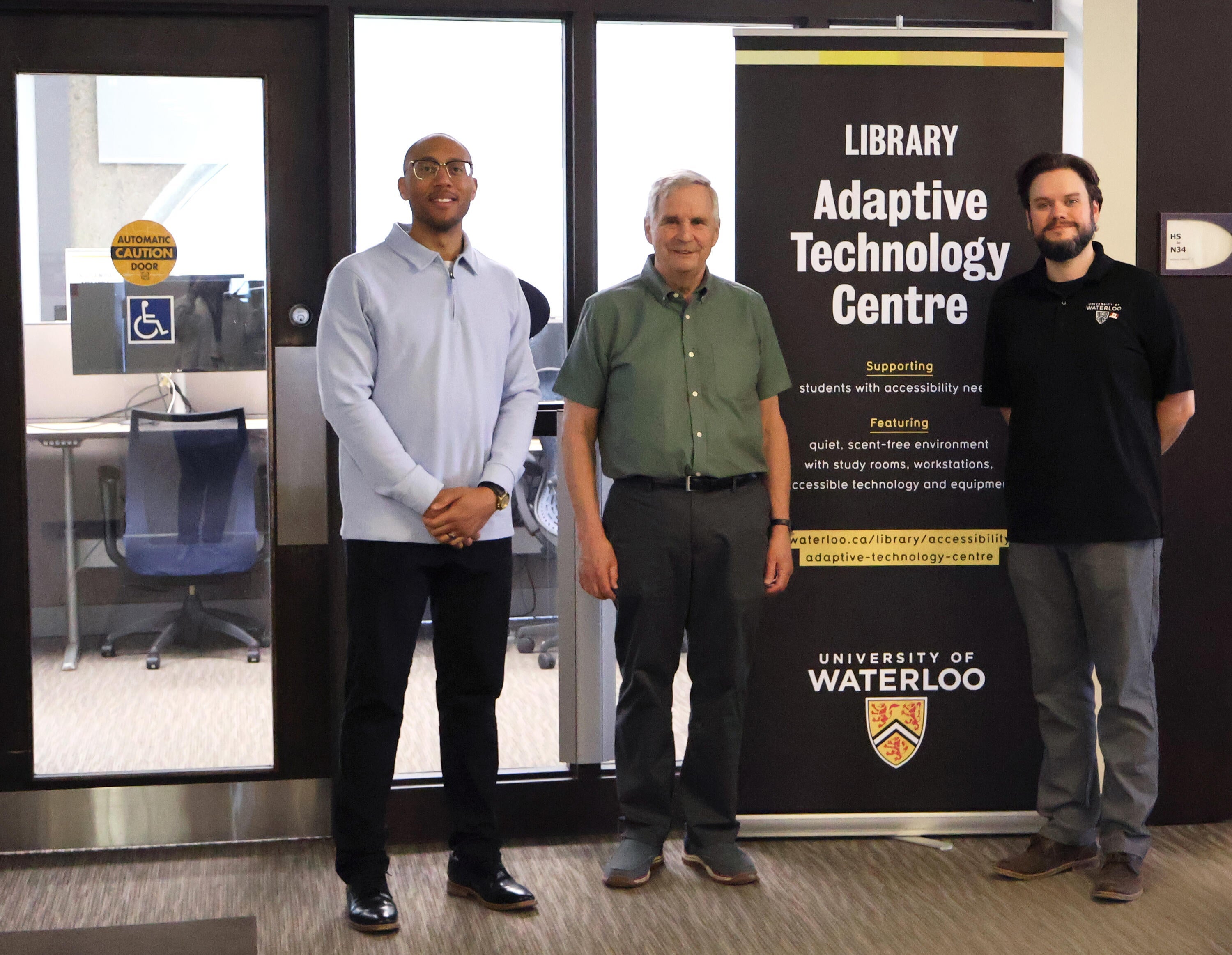 three people standing in front of a banner for the Adaptive Technology Centre in the Dana Porter Library