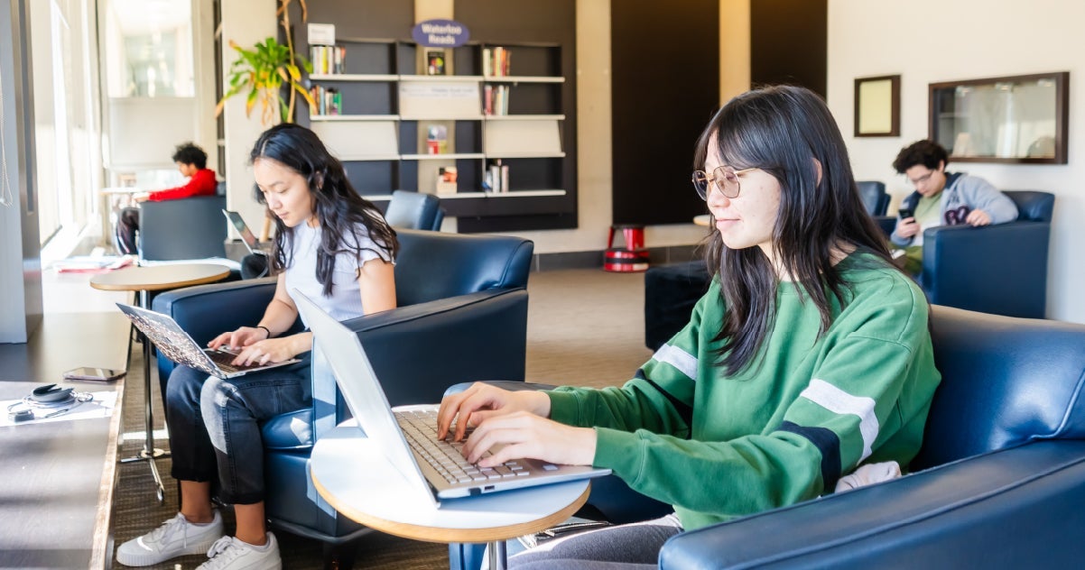 two students sitting while working on laptops at Dana Porter Library