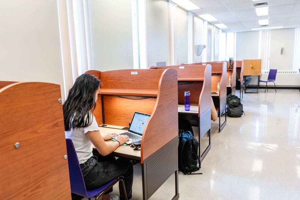 student sitting at a study carrel on a laptop inside Dana Porter Library